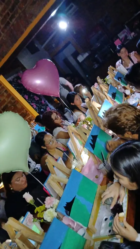 Mujeres pintando paisajes en lienzos pequeños, con globos de corazón